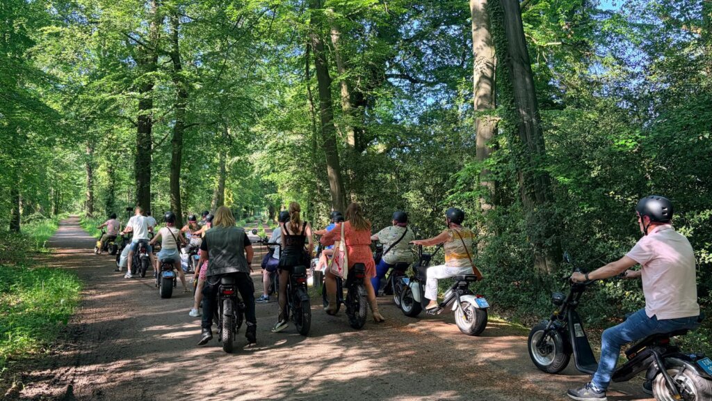 Groep op e-choppers rijdt over een bosweg tijdens een uitje vanaf De Weijenborg